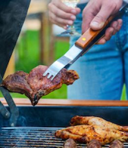 Barbecuing meat on grill. Close-up of two people barbecuing meat on the grill while standing outdoors