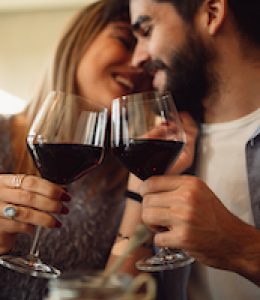 Couple clink glasses with red wine at date in casual outfit in cafe. Couple having romantic moments.