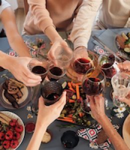 High angle view of people sitting at festive table having dinner and toasting with glasses of red wine